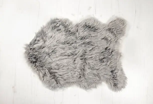 Flat lay view of gray warm and cozy whole decorative fake sheepskin shape rug on white wooden board floor.  Copy space, studio set.