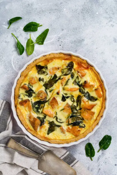 Homemade quiche tart with red fish and spinach on light wooden background. Vintage style. Top view.