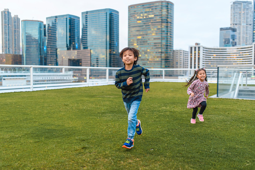 Young and energetic Chinese siblings running across grass at Ocean Terminal Deck atop Harbour City Shopping Centre in Hong Kong.