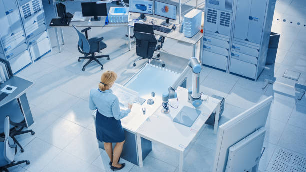 istock Stylish Female Industrial Robotics Engineer Looks at Blueprints Engineering Ways to Program and Manipulate Robot Arm for Lifting, Moving Objects. Technology Research Facility for Machine Learning 1173740510