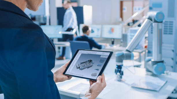 istock Stylish Female Industrial Robotics Engineer Uses Tablet Computer with CAD Software and to Manipulate and Program Robot Arm for Lifting, Moving Objects. Technology Research Facility for Cloud Computing 1173740530