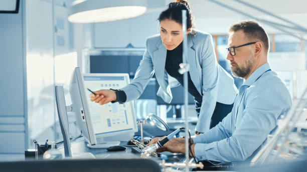 istock Female Chief Engineer Talks with Male Electronics Specialist, Explaining Things, He Works on Computer and Agrees with Her. Modern and Bright Office with Stylish People 1173740568