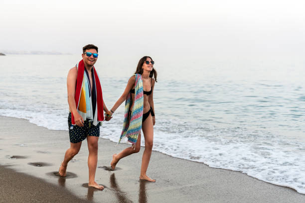 istock Relaxed couple holding hands and slowly walking along water shore 1173747406