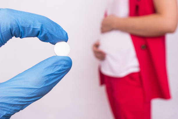 le médecin tient une pilule sous la forme d'un complexe de vitamines et d'acide folique sur le fond d'une fille enceinte, le manque de vitamines et de calcium pendant la grossesse - zinc mineral nutritional supplement pill photos et images de collection