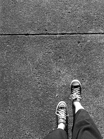 Black and white of woman walking footpath in converse all stars