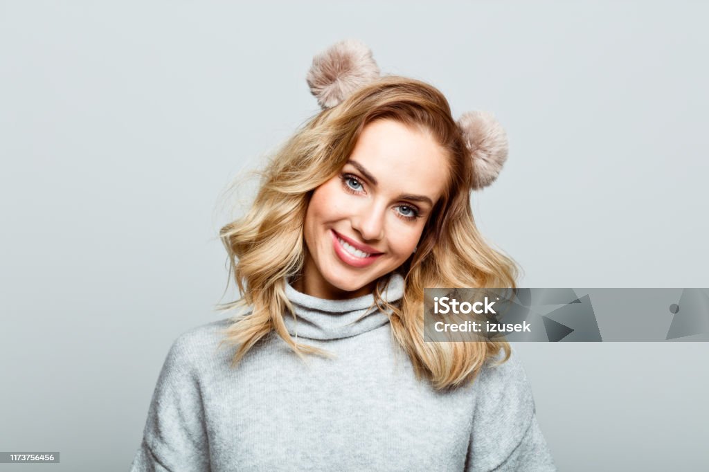Winter portrait of cute beautiful woman, close up of face stock photo Mid adult beautiful woman wearing sweater and hand band standing against grey background, smiling at camera. One Woman Only Stock Photo