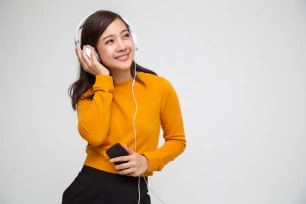 Photo of Young Asian beauty woman listening music with headphones in playlist song application on smartphone isolated on white background