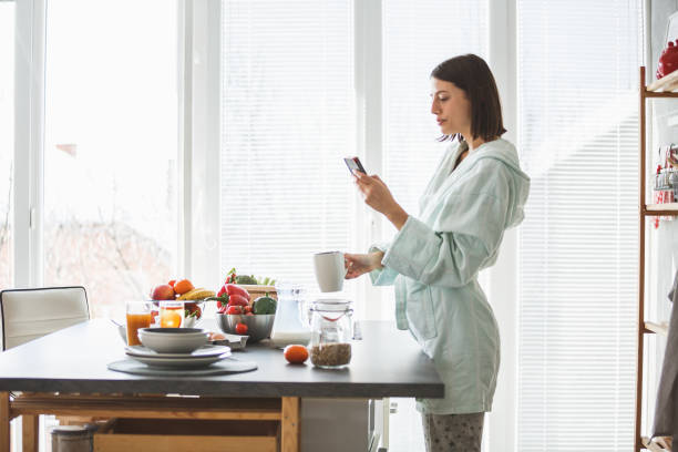 istock Young woman using smart phone and having morning tea at home 1173760208