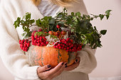 Closeup of autumn flowers and berries composition in pumpkin vase. Woman holding pumpkin decorated fort table setting and celebration. Autumn, Halloween, Thanksgiving.