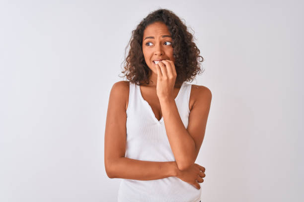 young brazilian woman wearing casual t-shirt standing over isolated white background looking stressed and nervous with hands on mouth biting nails. anxiety problem. - nail biting imagens e fotografias de stock