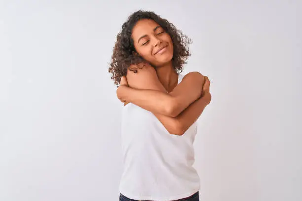 Young brazilian woman wearing casual t-shirt standing over isolated white background Hugging oneself happy and positive, smiling confident. Self love and self care