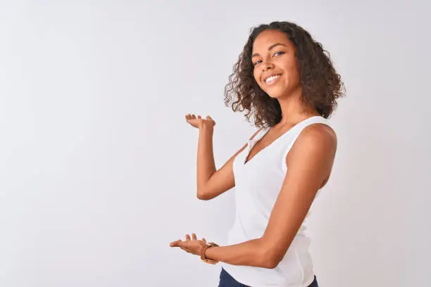Young brazilian woman wearing casual t-shirt standing over isolated white background Inviting to enter smiling natural with open hand