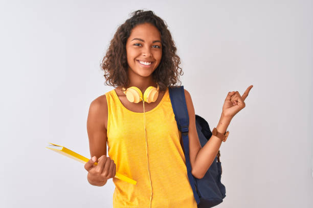 femme d'étudiant brésilien utilisant le sac à dos retenant le cahier au-dessus du fond blanc d'isolement très heureux pointant avec la main et le doigt au côté - spanish and portuguese ethnicity photos photos et images de collection