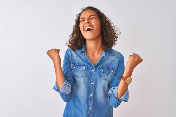young brazilian woman wearing denim shirt standing over isolated white background celebrating surprised and amazed for success with arms raised and eyes closed. winner concept. - teenager teenagers only one teenage girl only human face imagens e fotografias de stock