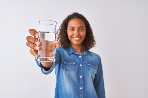 Young brazilian woman holding glass of water standing over isolated white background with a happy face standing and smiling with a confident smile showing teeth
