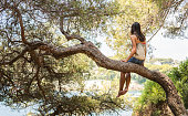 Young woman on tree looking at sea
