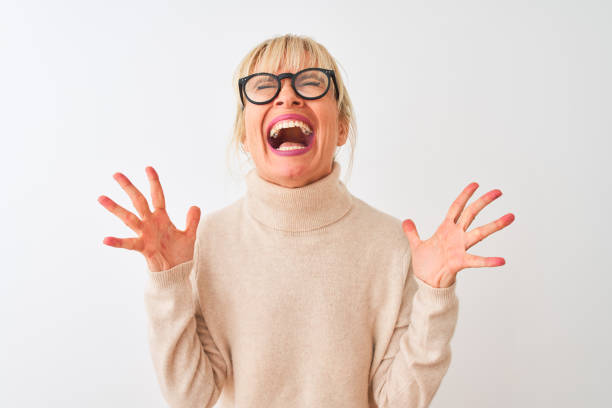средний возраст женщина носить водолазка свитер и очки на изолированном белом фоне празднования ума и сумасшедший для успеха с поднятыми р - cheerful women shouting happiness стоковые фото и изображения