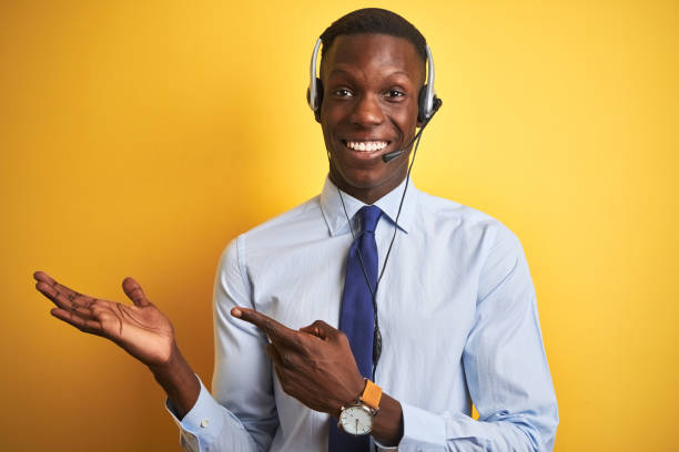 istock African american operator man working using headset over isolated yellow background amazed and smiling to the camera while presenting with hand and pointing with finger. 1173776971