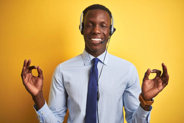 istock African american operator man working using headset over isolated yellow background relax and smiling with eyes closed doing meditation gesture with fingers. Yoga concept. 1173776991