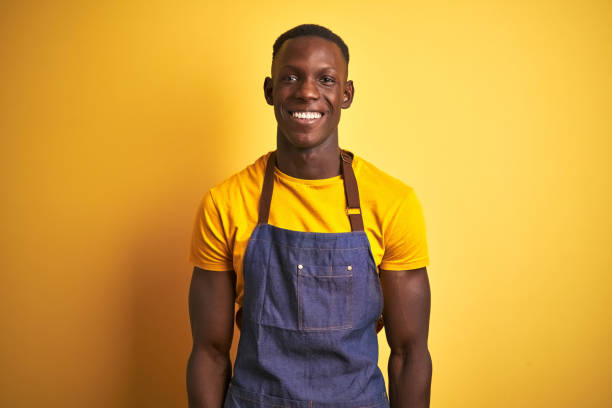 istock African american bartender man wearing apron standing over isolated yellow background with a happy and cool smile on face. Lucky person. 1173780192