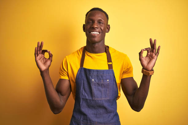 istock African american bartender man wearing apron standing over isolated yellow background relax and smiling with eyes closed doing meditation gesture with fingers. Yoga concept. 1173780202