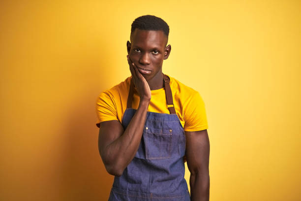 istock African american bartender man wearing apron standing over isolated yellow background thinking looking tired and bored with depression problems with crossed arms. 1173780209