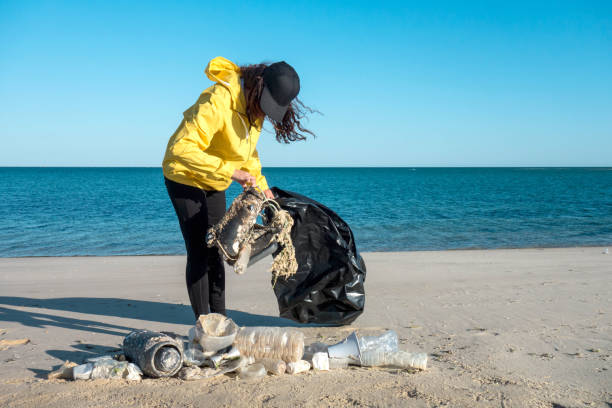 istock Woman picking up trash and plastics cleaning the beach with a garbage bag. 1173780233