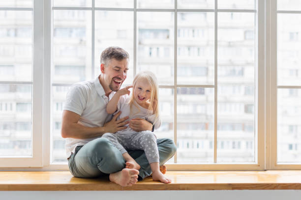 istock Happy father hugs daughter while sitting on window sill 1173781979