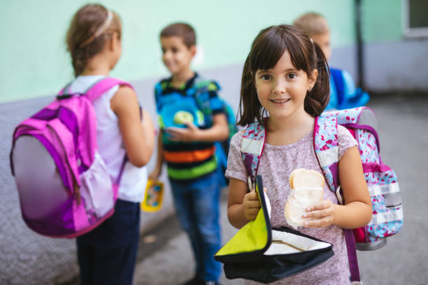 Little girl holding lunch box and eating sandwich in a school yard Little girl holding lunch box and eating sandwich in a school yard food elementary student healthy eating schoolboy stock pictures, royalty-free photos & images