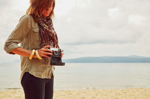 Fashionable woman holding camera on the beach.