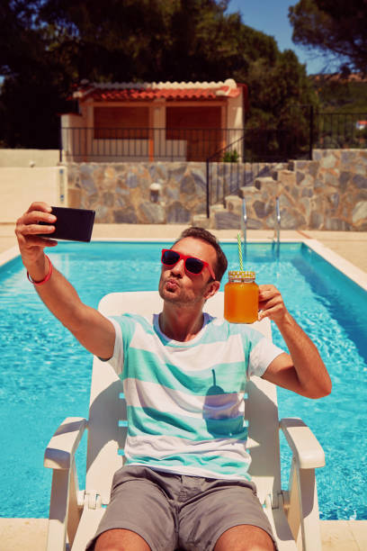 istock Attractive man using cellphone while drinking juice near swimming pool. 1173789573