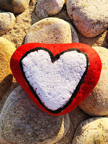 A pile of beach pebbles with a red heart painted on the top one