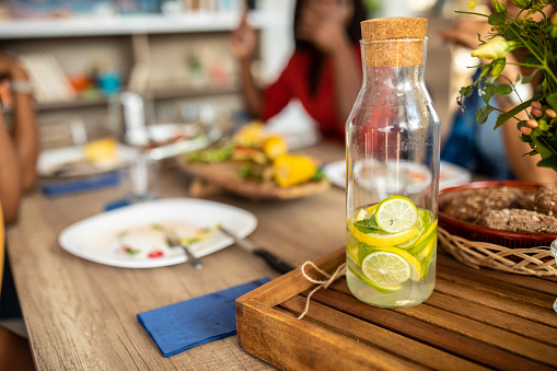 Lunch setting with fresh lemon juice, wooden table with plates, drinking glasses, lemonade, bread