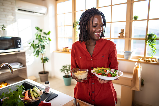 Smiling black   woman serving vegetarian meal to friends at home on  plate