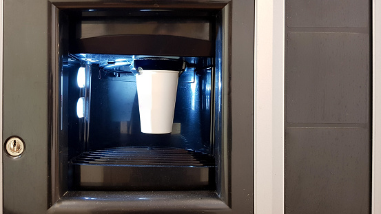 White paper cup in the window of a vending coffee machine. The process of making coffee in a wading