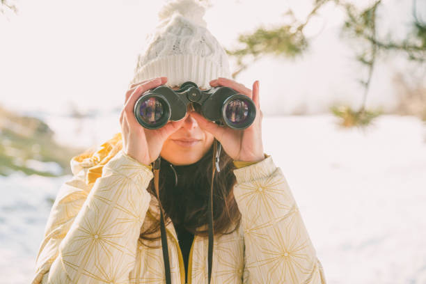 istock The girl in a White cap with a backpack in the winter in a forest looking through binoculars 1173803782