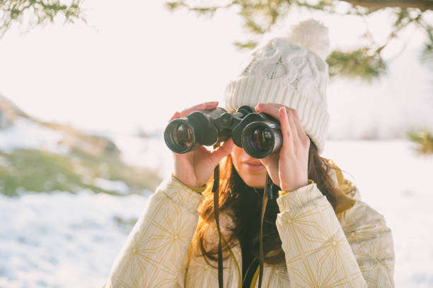 istock The girl in a White cap with a backpack in the winter in a forest looking through binoculars 1173803809