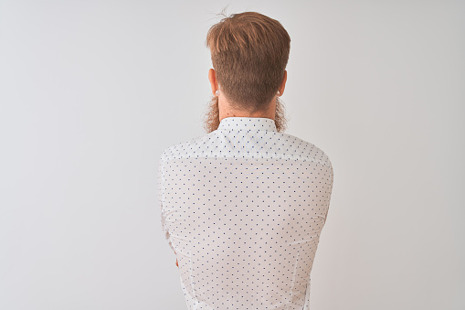 Young redhead irish businessman standing over isolated white background standing backwards looking away with crossed arms