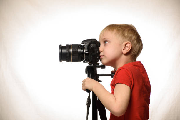 istock Blond boy takes pictures with a SLR camera. Side view. White background 1173812676