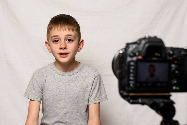 istock Schoolboy is saying something on a camcorder. Young video blogger. White background 1173812871