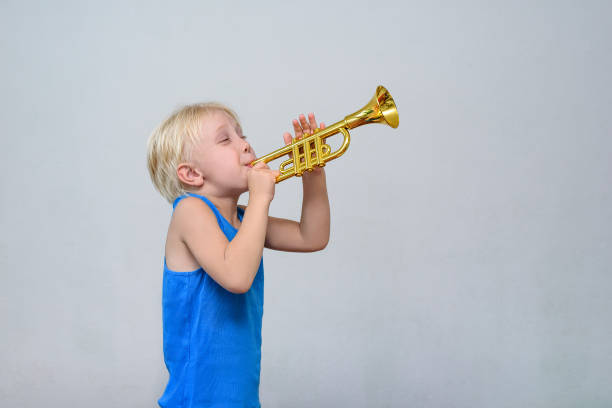 istock Little cute blond boy playing toy trumpet on light background 1173812924