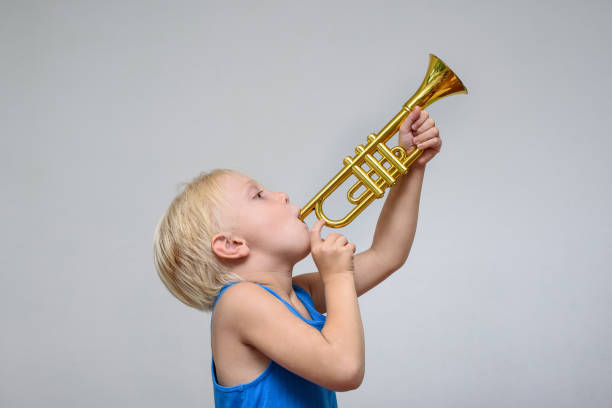istock Little cute blond boy playing toy trumpet on light background 1173812926