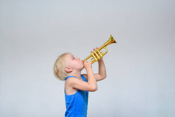 istock Little cute blond boy playing toy trumpet on light background 1173812933