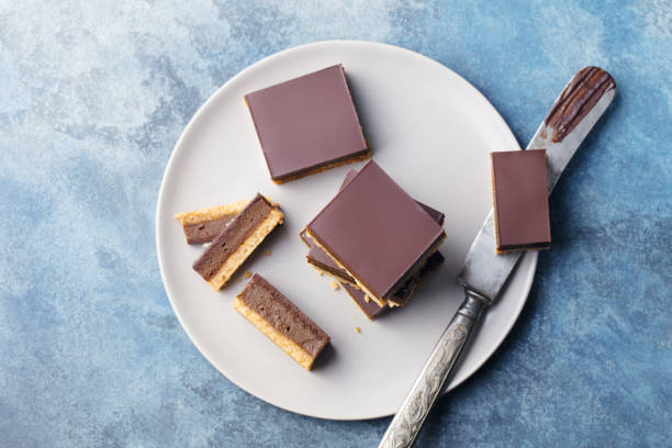 schokolade karamell scheiben, bars, millionäre kurzbrot auf einem teller. blauer hintergrund. ansicht von oben. - shortbread caramel chocolate candy biscuit stock-fotos und bilder