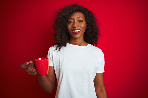 Young african american woman drinking cup of coffee over isolated red background with a happy face standing and smiling with a confident smile showing teeth