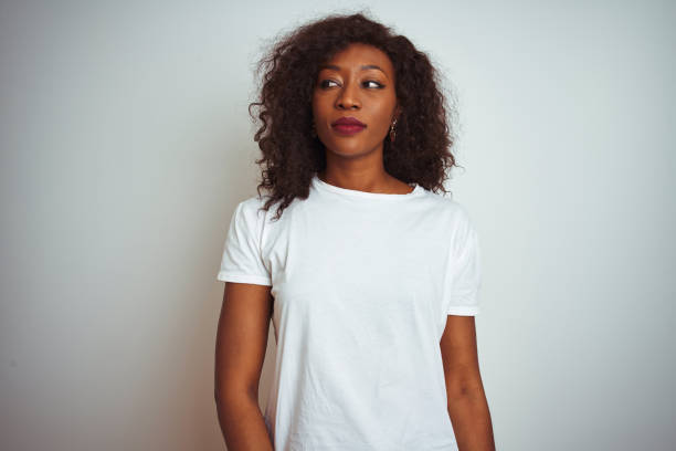 young african american woman wearing t-shirt standing over isolated white background smiling looking to the side and staring away thinking. - mannered imagens e fotografias de stock