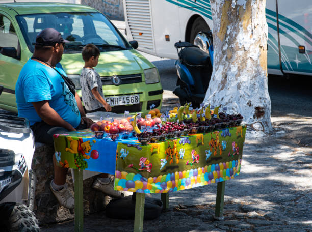 un vendeur de fruits avec un stand coloré juste à côté de la gare routière centrale de fira près de la rue mirtropoleos - greek culture greek flag greece little boys photos et images de collection