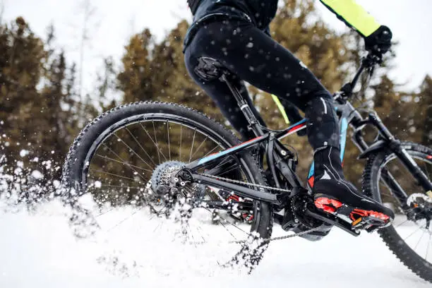 Photo of Midsection of mountain biker riding in snow outdoors in winter.