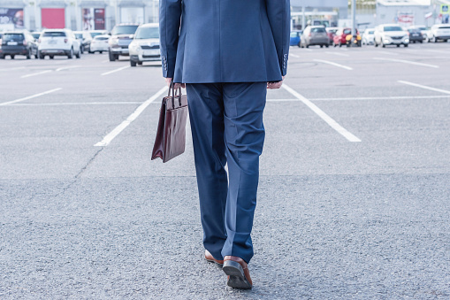 Businessman in blue suit and brown briefcase on the outdoor car parking .