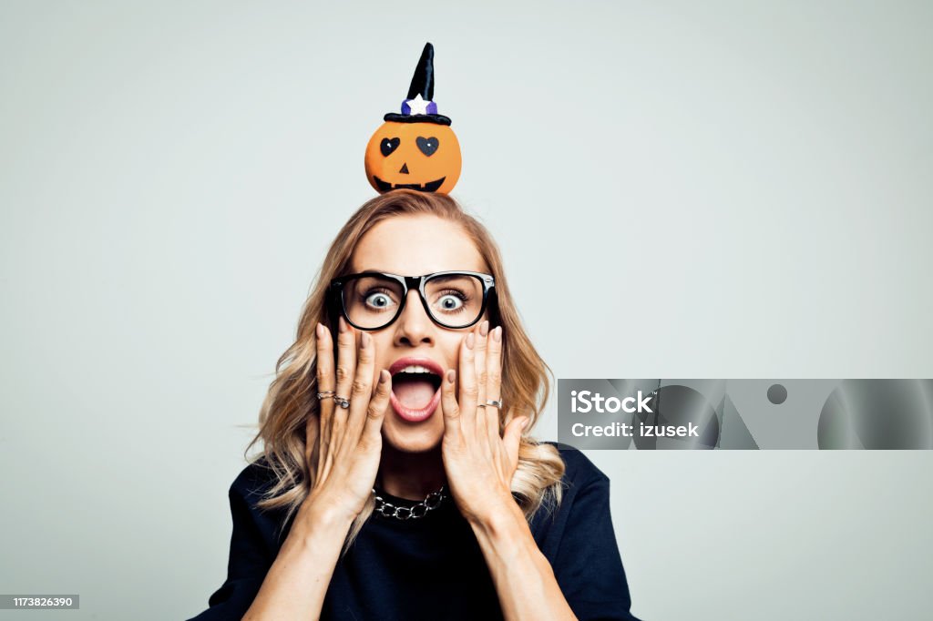 Shocked woman ready for halloween, stock photo Mid adult beautiful woman wearing black sweater and headband with pumpkin standing against grey background and shouting at camera. Pumpkin Stock Photo